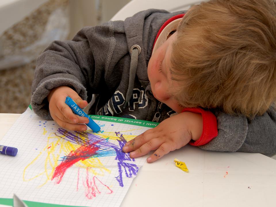 Un bambino disegna con i colori dell'arcobaleno